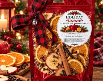 May include: A red pouch containing dried apple slices, orange slices, cinnamon sticks, and cloves. The pouch features a red and black buffalo plaid ribbon with a silver bell and a label reading Holiday Simmer Stovetop Potpourri.
