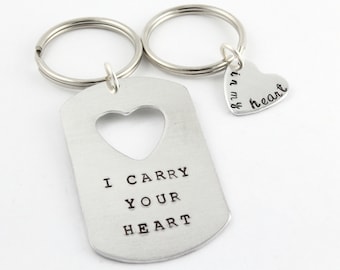 May include: Two silver keychains with a heart-shaped cutout. One keychain has the text "I carry your heart" and the other keychain has the text "in my heart".
