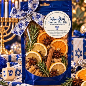 May include: A blue pouch labeled Hanukkah Simmer Pot Kit containing dried orange slices, cinnamon sticks, star anise, cloves, and rosemary sprigs. The pouch is tied with a blue and silver snowflake ribbon and a silver Star of David charm.