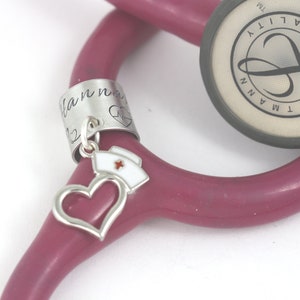 Silver stethoscope charm with silver heart and nurse hat charm dangling from the bottom center of the tag.