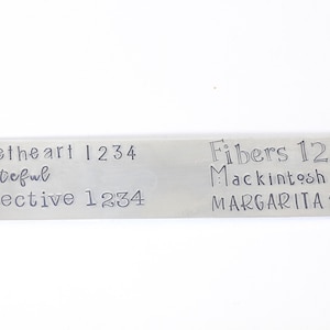 May include: A silver metal tag with engraved text. The text reads "Sweetheart 1234 grateful Detective 1234" on the left side and "Fibers 1234 Macintosh 1234 MARGARITA 1234" on the right side.