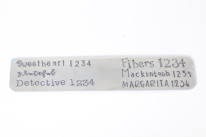 May include: A silver metal tag with engraved text. The text reads "Sweetheart 1234 grateful Detective 1234" on the left side and "Fibers 1234 Macintosh 1234 MARGARITA 1234" on the right side.