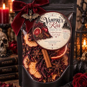 May include: A black pouch containing a Vampire's Kiss simmer pot kit, featuring dried blood orange slices, apple slices, hibiscus petals, cinnamon sticks, and star anise. A dark red velvet bow with a metal bat charm is attached to the top.