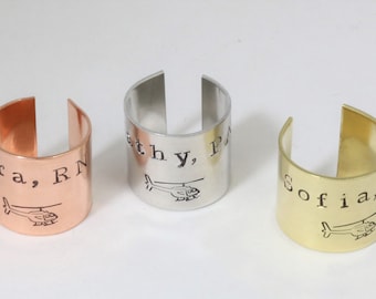 May include: Three personalized metal rings with engraved names and a helicopter graphic. The rings are in copper, silver, and gold.