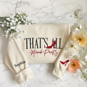 May include: A white ceramic mug with a black handle and the text "But First, Coffee" in a bold, black font. The mug is set against a neutral background, highlighting its simple design.