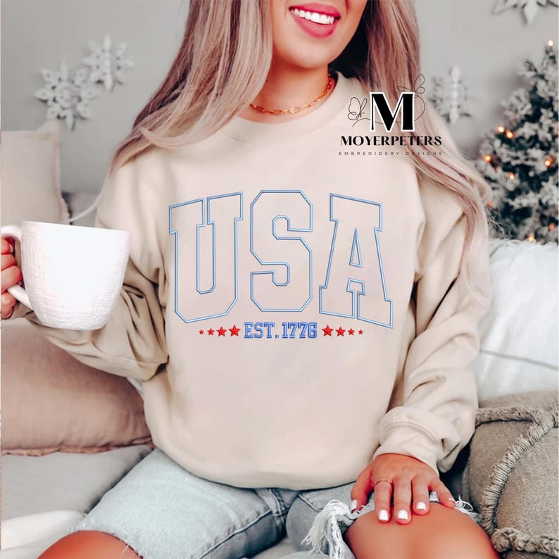 May include: A beige sweatshirt with a white graphic of "USA EST. 1776" with blue outlines and red stars.