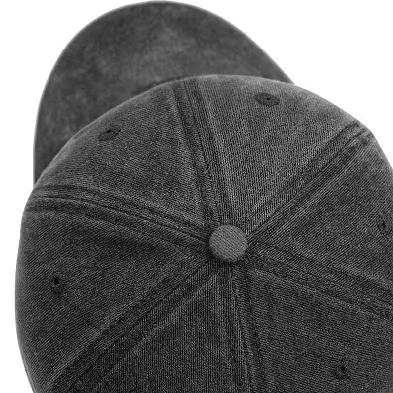 May include: A charcoal grey baseball cap with a washed, distressed texture. The cap features a six-panel construction with stitched seams, a fabric-covered button at the crown, and small embroidered eyelets for ventilation on each panel.