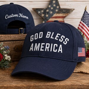 Puede incluir: Gorra de béisbol azul marino con la frase "GOD BLESS AMERICA" bordada en blanco. Cuenta con un parche de la bandera estadounidense y "Custom Name" en la parte trasera. Correa ajustable. Tema patriótico.