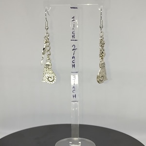 May include: Silver-toned cat earrings hanging from a clear display stand. The earrings are approximately 2 inches long and feature a detailed cat charm. The stand has inch markings for size reference. The earrings are displayed on a black surface.