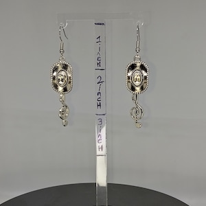 May include: Silver dangle earrings with a cowboy hat charm and a treble clef charm. The earrings are approximately 2 inches long.