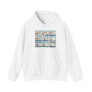 Pode incluir: Uma camisola branca de manga comprida com capuz, apresentando uma impressão gráfica central composta por nove painéis quadrados individuais. A ilustração mostra uma pessoa a interagir com um cavalo castanho em vários cenários ao ar livre.