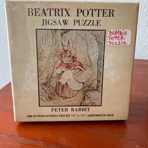 May include: A vintage Beatrix Potter jigsaw puzzle box. The box features an illustration of Peter Rabbit holding a basket. The text on the box reads "BEATRIX POTTER JIGSAW PUZZLE" and "PETER RABBIT". The assembled size is 7.5" x 7.5".