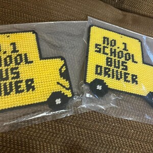 May include: Two yellow school bus keychains with black lettering that reads "No. 1 School Bus Driver". The keychains are packaged in clear plastic bags.