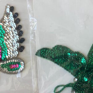 May include: Two butterfly-shaped sequin appliques. One butterfly features wings with pink, green, and gold sequins, and black accents. The other butterfly has green sequin wings.