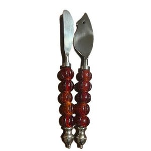 May include: A set of two stainless steel cheese knives with red and amber glass bead handles.