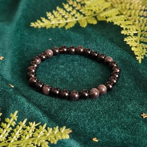 May include: A stretch bracelet composed of smooth, round beads in shades of deep black and muted charcoal grey. The beads are arranged in a circular pattern, featuring a polished finish that reflects light across the surface of each individual stone.