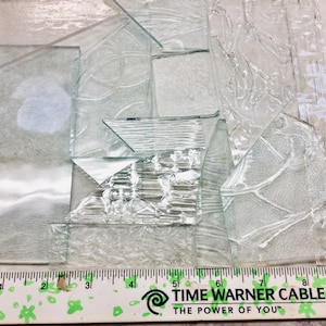 May include: A collection of clear glass pieces with various textures and patterns. The glass pieces are arranged on a white surface with a ruler at the bottom. The ruler is labeled "TIME WARNER CABLE THE POWER OF YOU".