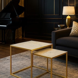 May include: Two square nesting tables. They have gold metal frames and white marble tops. The tables are on a grey rug. The room has dark walls, a grand piano, a lamp and a sofa. The tables are a stylish addition.