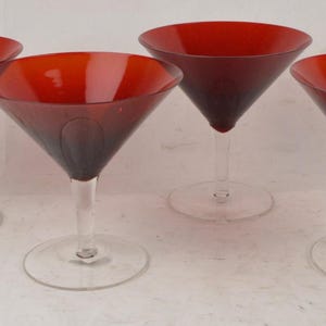 May include: A set of four martini glasses featuring deep red, conical bowls and clear glass stems and circular bases. Each glass has a wide, open rim and a smooth, tapered design, providing a consistent look across the entire collection of glassware.