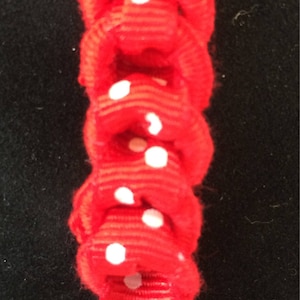 Può includere: Nastro rosso con pois bianchi, annodato in una serie di anelli. Il nastro si staglia su uno sfondo nero, creando un contrasto sorprendente. Il design è semplice ma accattivante.