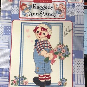May include: Cross stitch pattern featuring Raggedy Andy holding a bouquet of flowers. The pattern is titled "With Love, Raggedy Andy" and is from the "Classic Raggedy Ann & Andy" collection. The pattern number is RA104.