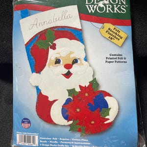 Op de afbeelding: Een Design Works vilten kousenkit met een ontwerp van de kerstman en poinsettia's. De kit bevat bedrukte vilt- en papieren patronen, pailletten, katoenen draad, kralen en een naald. De afgewerkte kous meet 45.7 cm.