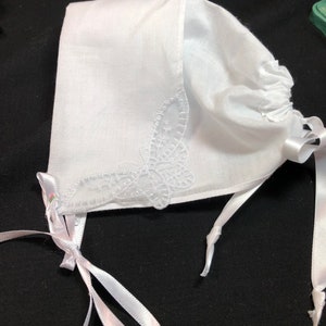 Peut inclure: Bonnet en coton blanc avec un délicat motif de papillon brodé et des rubans en satin blanc.