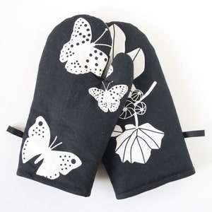 May include: A pair of black oven mitts with a white butterfly and leaf design.