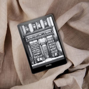 May include: A black and white illustration of a bookstore storefront is displayed on a Kindle e-reader. The e-reader is lying on a beige fabric surface.