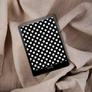 May include: A black and white e-reader with a floral pattern on the screen. The screen displays the word "kindle".