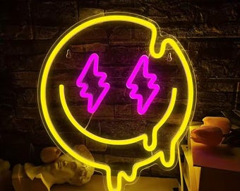 May include: A neon sign in the shape of a yellow smiley face with melting edges. The eyes are two pink lightning bolts. The sign is mounted on a dark brick wall. The sign is lit up and ready to hang.
