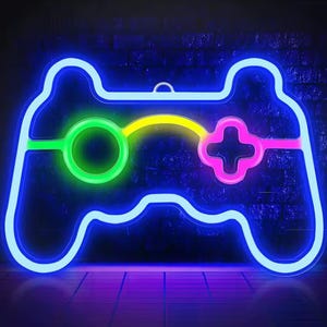 Può includere: Un'insegna al neon a forma di controller per videogiochi. Il contorno è blu brillante, con accenti verdi, gialli e rosa per i pulsanti e il D-pad. Lo sfondo è un muro di mattoni blu scuro.