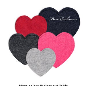 May include: An assortment of heart-shaped fabric patches in shades of red, navy, grey, pink, and light grey. The navy heart displays the text "Pure Cashmere". The text "More colours & sizes available" is at the bottom of the image.
