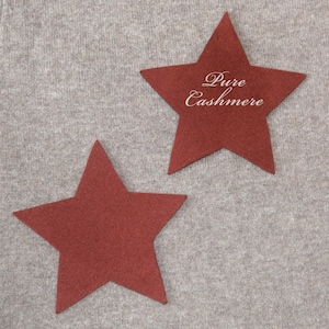 May include: Two red star-shaped patches on a light gray background. One star has the words "Pure Cashmere" in a cursive font. The stars are a solid color and appear to be made of a soft material, possibly felt or fabric.