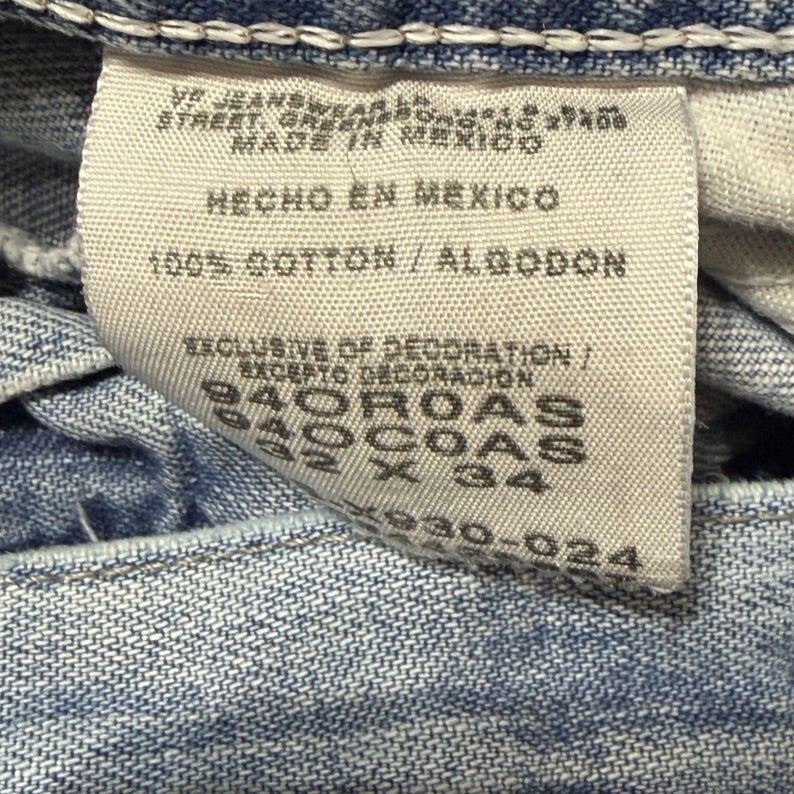 May include: Close-up of a light blue denim jeans label. The label includes text in English and Spanish, such as "Made in Mexico" and "100% Cotton". The label also has size information.
