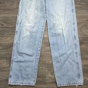 May include: Light blue denim jeans with a faded wash. The jeans have a classic five-pocket design, a straight leg, and a button and zipper closure. The jeans are made of a durable denim material and are suitable for everyday wear.