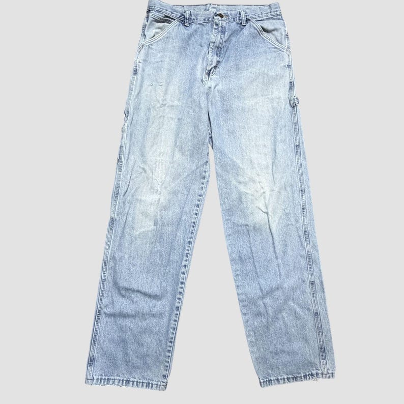 May include: Light blue denim work pants with multiple pockets and a relaxed fit. The jeans have a faded wash and a classic five-pocket design, suitable for casual wear.