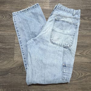 May include: Light blue denim work pants with multiple pockets and a relaxed fit. The jeans have a classic five-pocket design, with additional utility pockets on the legs. The denim is faded, giving the pants a worn-in look.