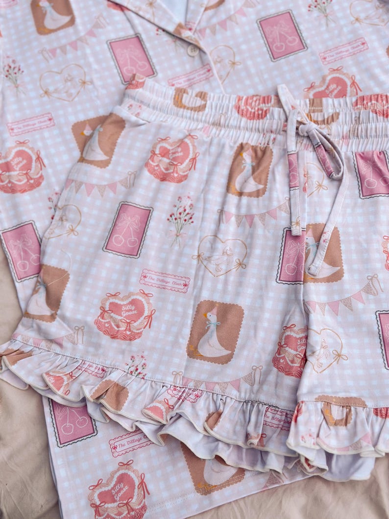 Puede incluir: Conjunto de pijama rosa y blanco con estampado de cuadros vichy y estampado de ganso. El conjunto incluye una parte superior de manga corta con cierre de botones en la parte delantera y un pantal&oacute;n corto con dobladillo con volantes.