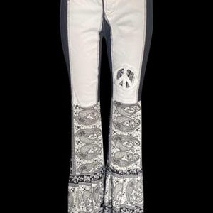 May include: White and black flared jeans with a peace sign detail. The jeans have a white front panel, black side panels, and a paisley print at the hem. The peace sign is cut out of the white panel on the right knee.