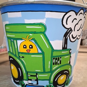 May include: A hand-painted metal bucket with a whimsical farm theme. The bucket features a bright green tractor with a yellow chick driver against a blue sky background. The tractor has black tires with yellow centers. A white cloud of smoke rises from the tractor's exhaust.