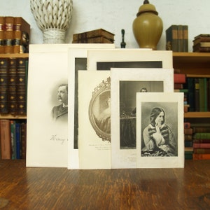 May include: Five black and white framed portraits of historical figures. The portraits are arranged in a row on a wooden surface. The portraits are of Henry Wadsworth Longfellow, Mary Ann Evans, Charles Dickens,  and  another unidentified person. The portraits are all in black and white and have a vintage look.