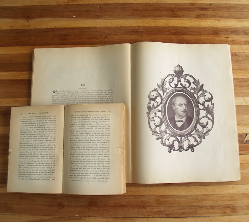 May include: Two open books with a brown wooden background. The book on the left has the title "The Holy Scripture" and the book on the right has the title "Revolution in the Nineteenth Century". The book on the right has a black and white portrait of a man in a decorative frame.