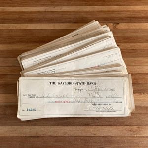 May include: A stack of vintage bank checks from The Gaylord State Bank, with handwritten details including the payee, amount, and date. The checks are on aged paper, with the check number 16545 visible.