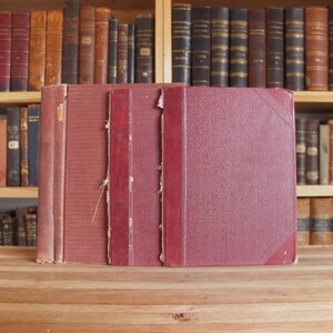 May include: Four burgundy-colored hardcover books with gold lettering on the spines. The books are stacked on a wooden surface.