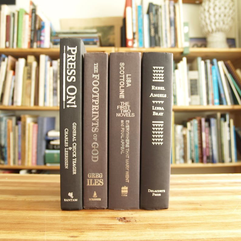 May include: Four hardback books with black covers and white text titles. The titles are "Press On!" by General Chuck Yeager and Charles Leerhsen, "The Footprints of God" by Greg Iles, "Lisa Scottoline The First Two Novels Everywhere That Mary Went and Final Appeal" and "Rebel Angels Libra Bray" by  Delacorte Press.