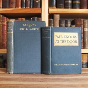 May include: Two vintage hardcover books with blue covers. The book on the left is titled "Sermons by John E. Hazelton". The book on the right is titled "Fate Knocks at the Door by Will Levinton Comfort".