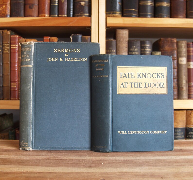 May include: Two vintage hardcover books with blue covers. The book on the left is titled "Sermons by John E. Hazelton". The book on the right is titled "Fate Knocks at the Door by Will Levinton Comfort".