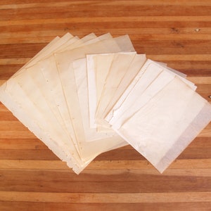 May include: A collection of rectangular sheets of off-white, semi-transparent paper arranged in a fanned-out stack. The paper has a smooth, thin texture with slightly uneven edges, displaying a light cream colour throughout the layered stack.
