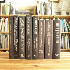 May include: A row of ten hardback books with black covers and silver lettering. The titles include "The Bucolic Plague", "Masters of the Macabre", "Baldacci | The Simple Truth", "Lotte Lehmann", "Press On!", "The Footprints of God", "Scottoline", "Lisa Scottoline", "Angel", and "Reel"